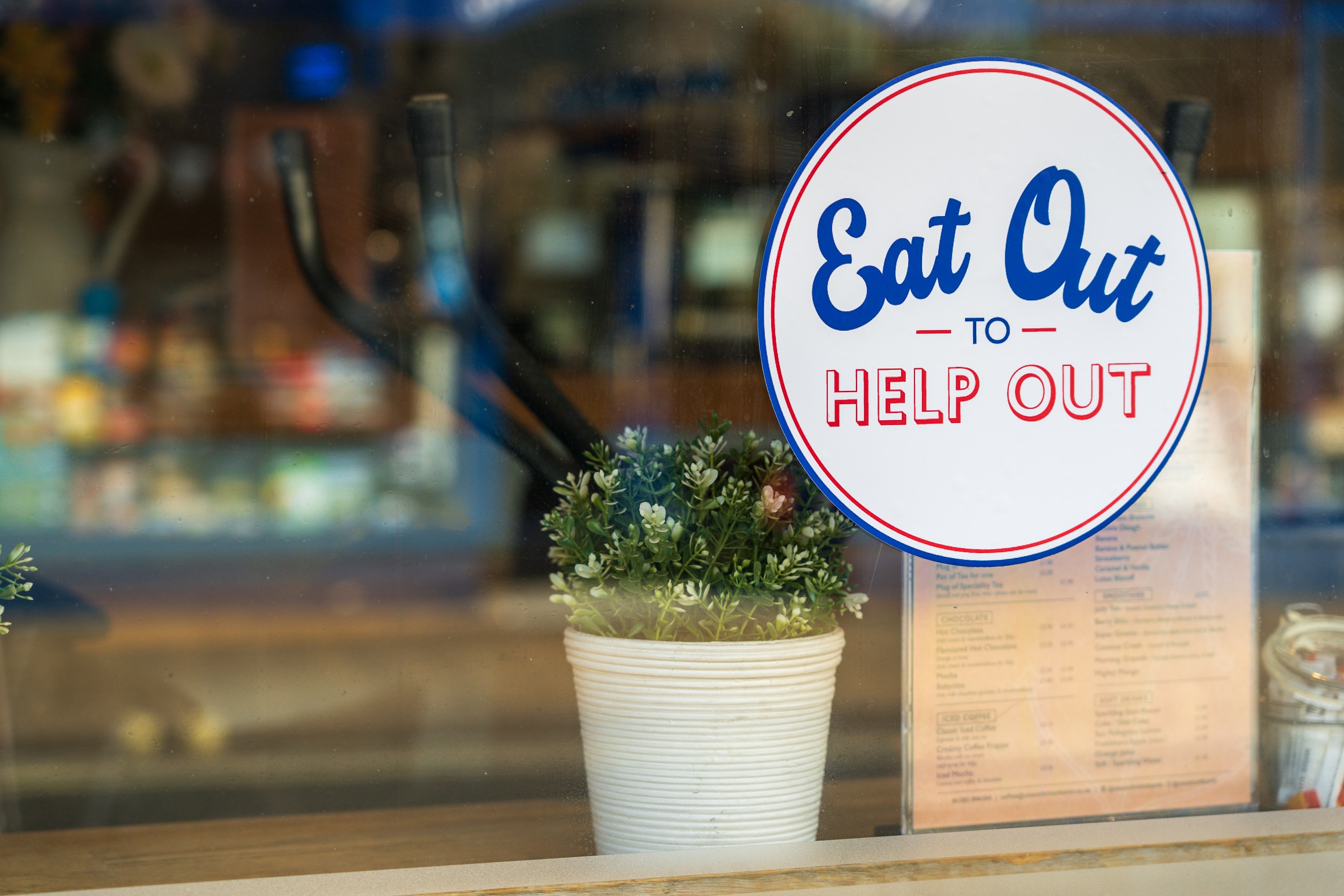A photograph of a café window displaying the 'Eat Out to Help Out' logo